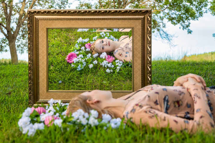 Kvinne ligger i gresset og ser i et speil